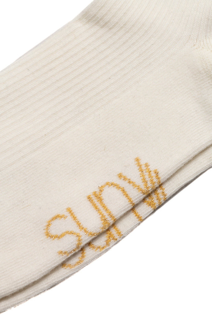 Chaussettes Ginette en coton bio écru, hauteur 10,5 cm, avec deux bandes dorées pailletées et broderie Suny sous le pied